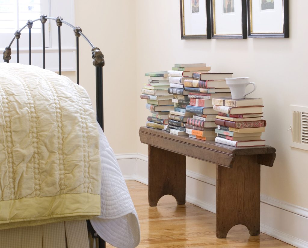 Stacks of books on a wooden bench in a bedroom