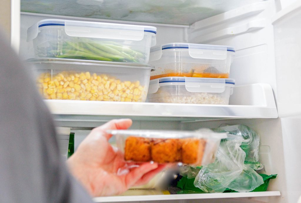 Open refrigerator showing organized food containers with a person holding packaged food in the foreground