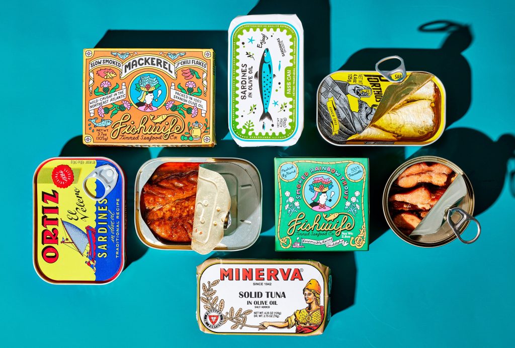 Various types of tinned fish products arranged on a surface with colorful packaging