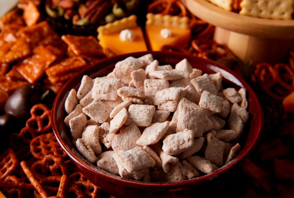 Bowl of powdered snack mix surrounded by various party snacks on a table
