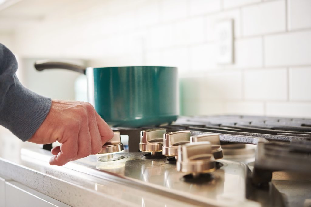 Unidentifiable middle aged man at gas stove in a modern bright white kitchen