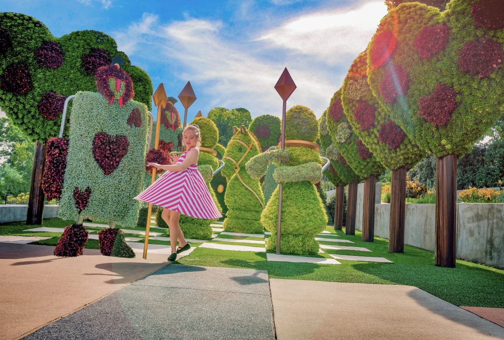 A child twirls in a striped dress surrounded by garden sculptures shaped like playing card characters