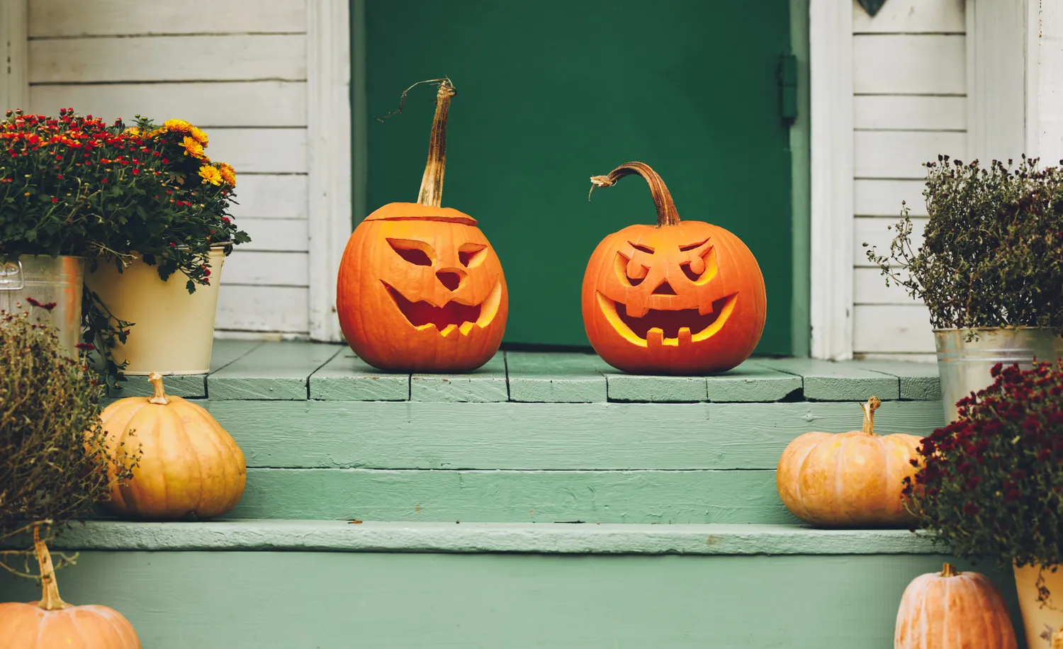 Two carved pumpkins on green steps surrounded by autumn decorations
