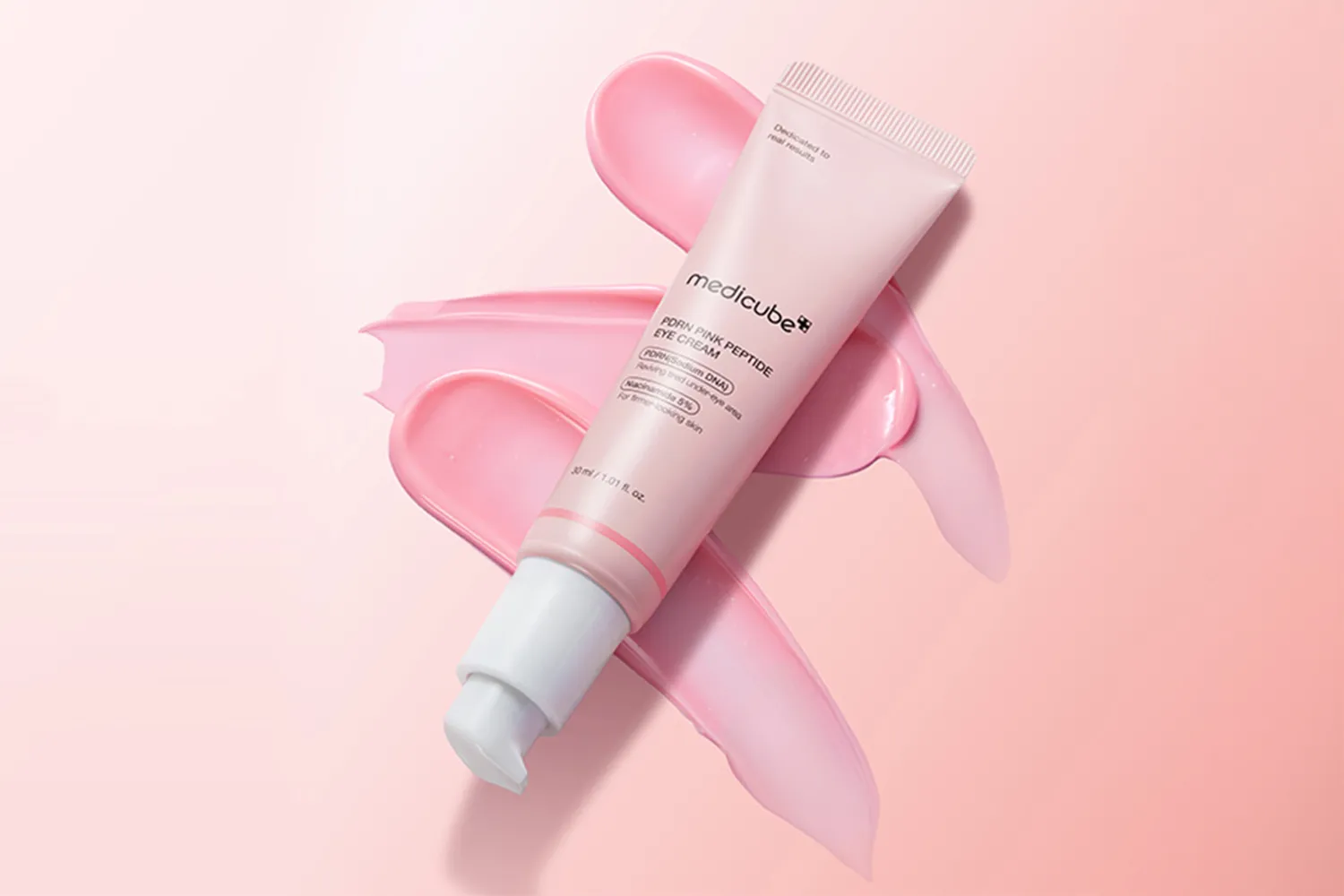 A tube of Medicube Pink Peptide Eye Cream placed on a background with smears of cream