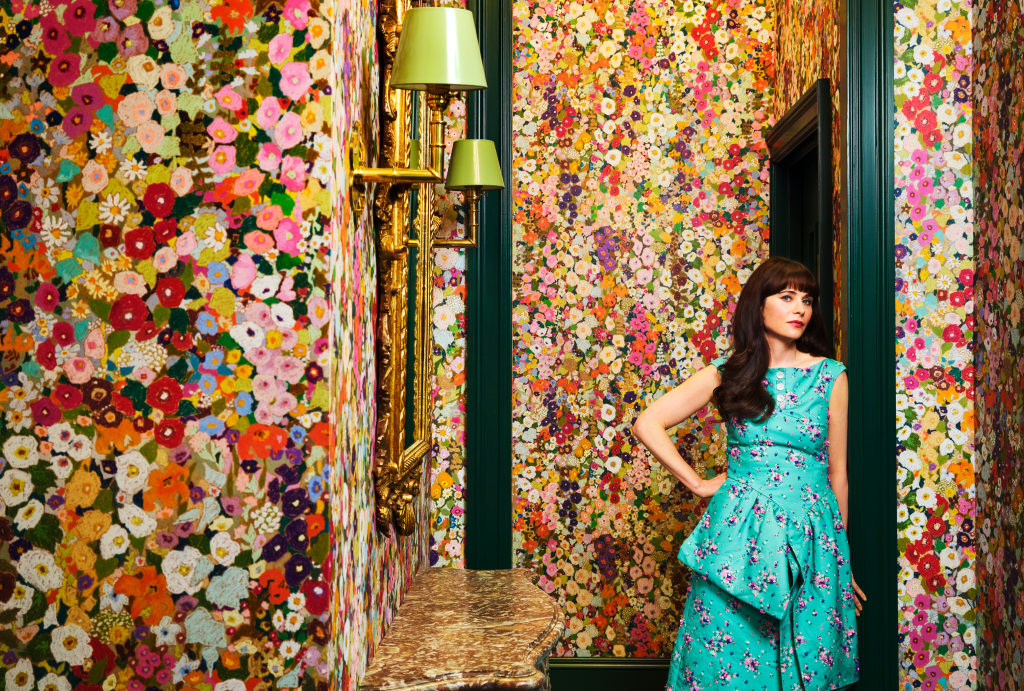 Zooey Deschanel standing in a floral wallpapered room