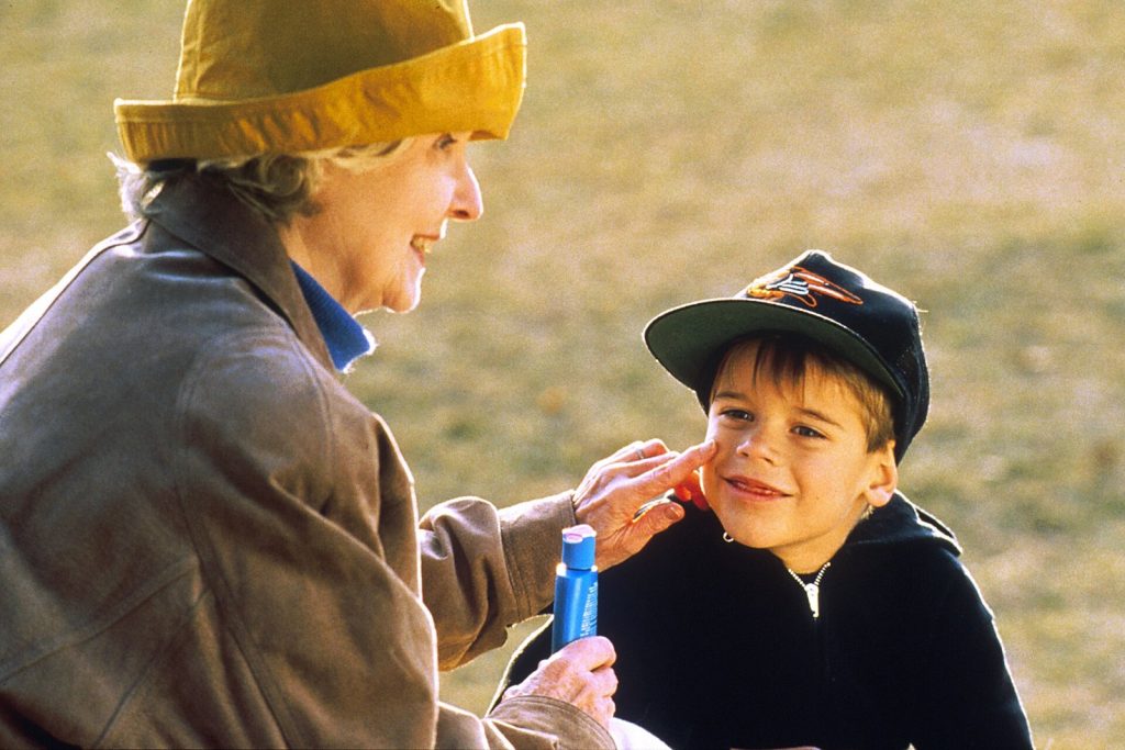 Adult applying a blue skincare product to a young boy’s cheek