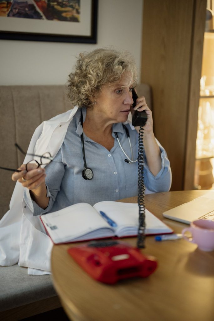 Woman physician in a white coat holding a corded telephone and eyeglasses