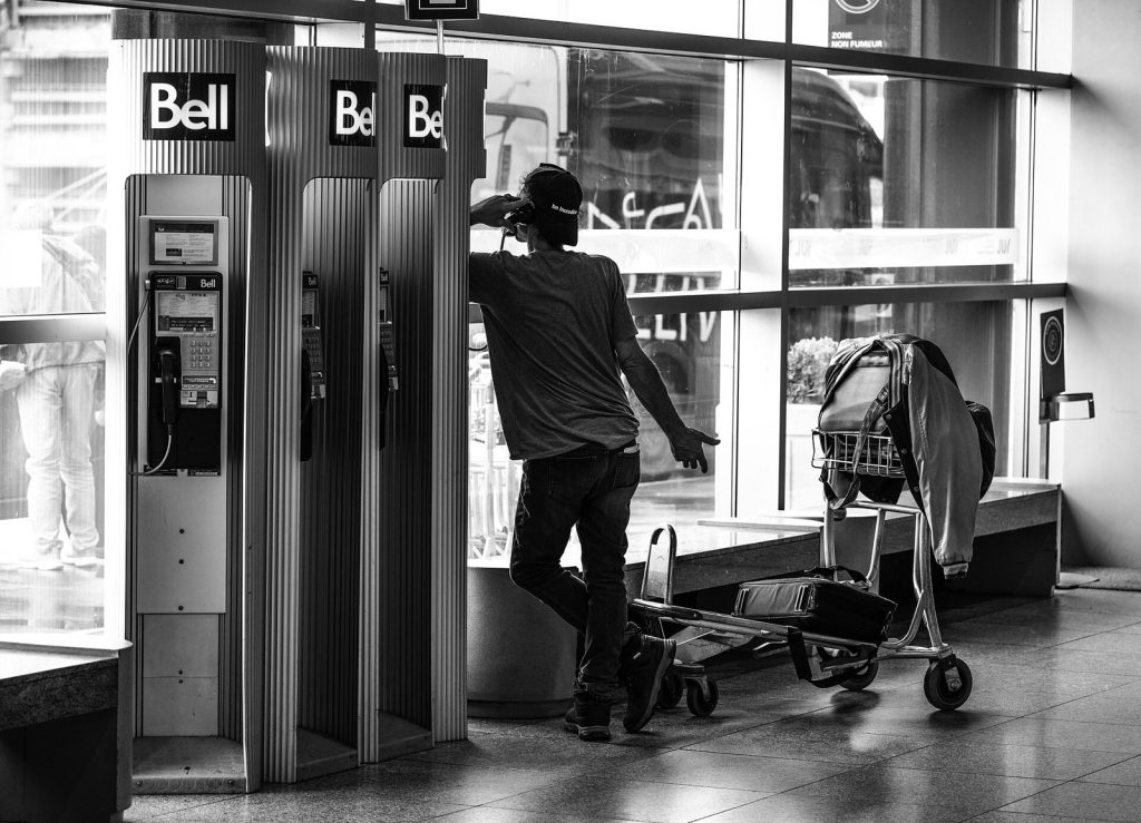 Man using a Bell public telephone beside a luggage cart